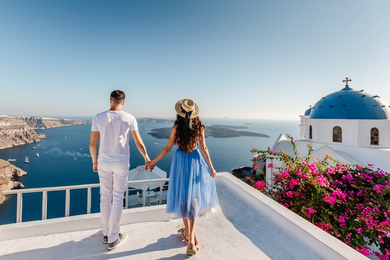 Young,Couple,Holding,Hands,And,Enjoying,View,On,Santorini,Island,