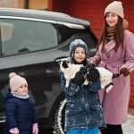 Kids with cat on hands against car in the yard of house at winte