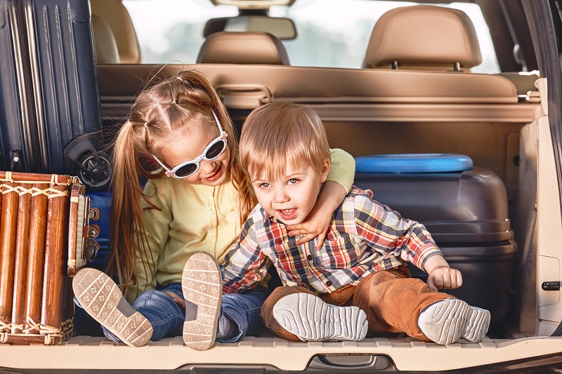 Beginning of the trip. Little cute kids in the trunk of a car with suitcases. Family road trip