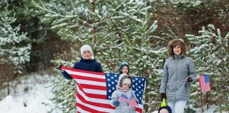 Family with four kids holding flag of USA on winter landscape.