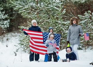 Family with four kids holding flag of USA on winter landscape.