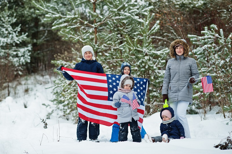 Family with four kids holding flag of USA on winter landscape.