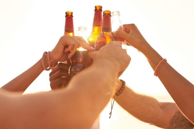 Friends clinking beer bottles in sunlight