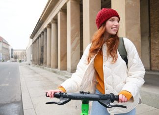 Young smiling redhead girl, student rides electric scooter, rents it and travels around city