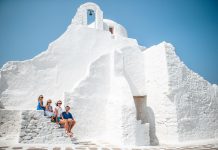 Family vacation in Europe. Parents and kids at street of typical greek traditional village with white walls and colorful doors on Mykonos Island