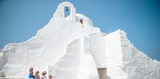 Family vacation in Europe. Parents and kids at street of typical greek traditional village with white walls and colorful doors on Mykonos Island