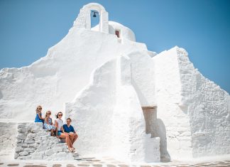 Family vacation in Europe. Parents and kids at street of typical greek traditional village with white walls and colorful doors on Mykonos Island