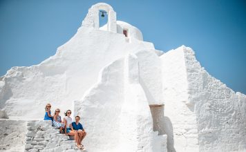 Family vacation in Europe. Parents and kids at street of typical greek traditional village with white walls and colorful doors on Mykonos Island