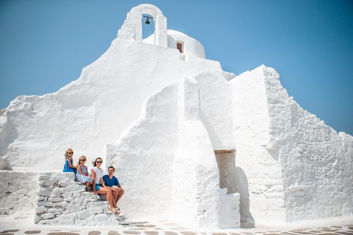 Family vacation in Europe. Parents and kids at street of typical greek traditional village with white walls and colorful doors on Mykonos Island