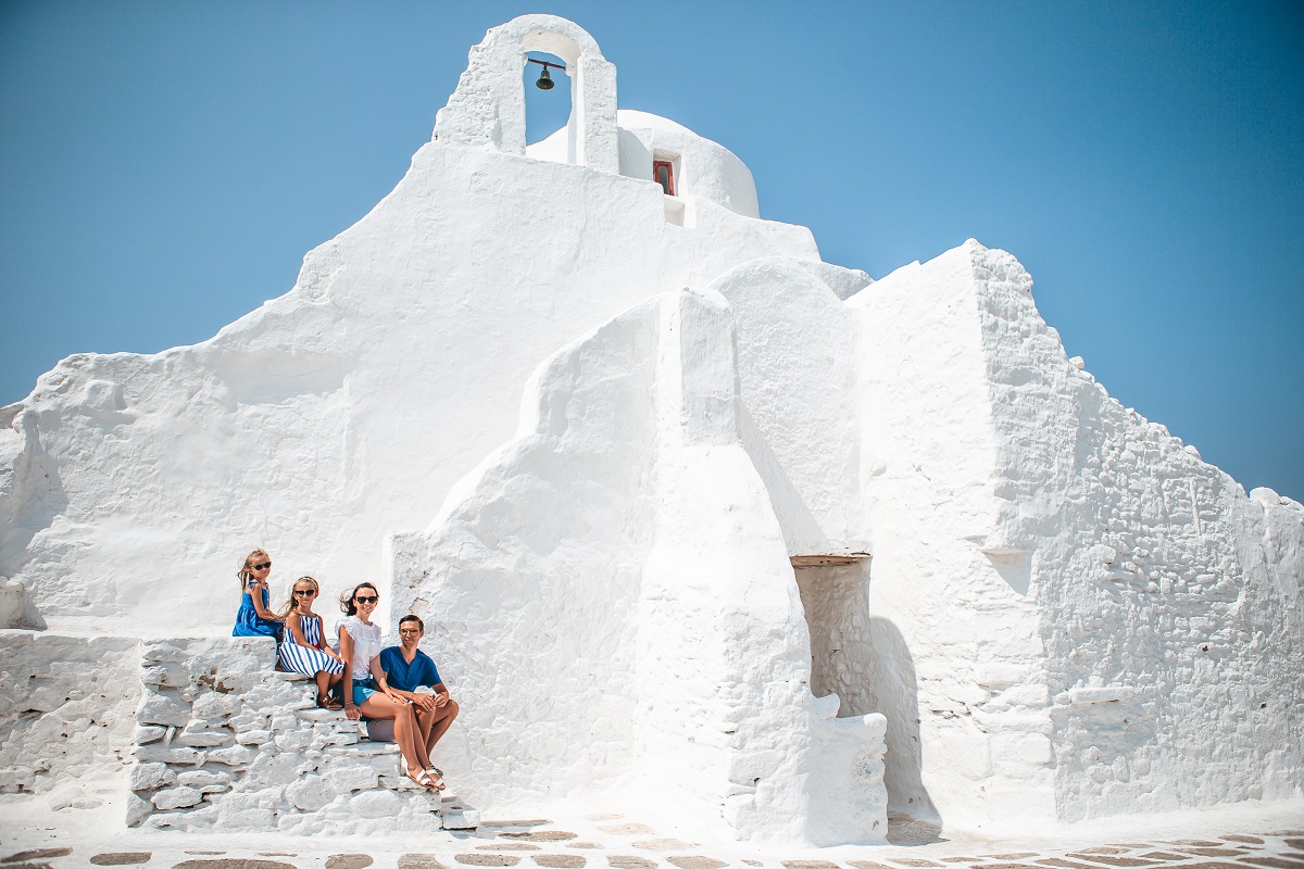 Family vacation in Europe. Parents and kids at street of typical greek traditional village with white walls and colorful doors on Mykonos Island